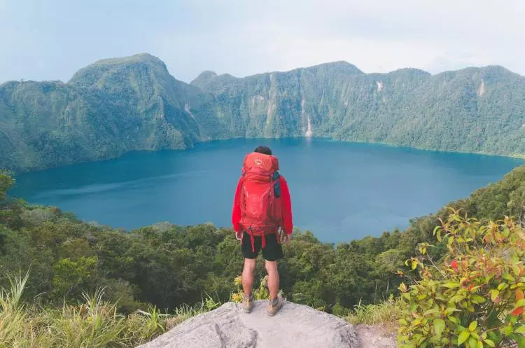 Man with red bag looking over lake and hills.