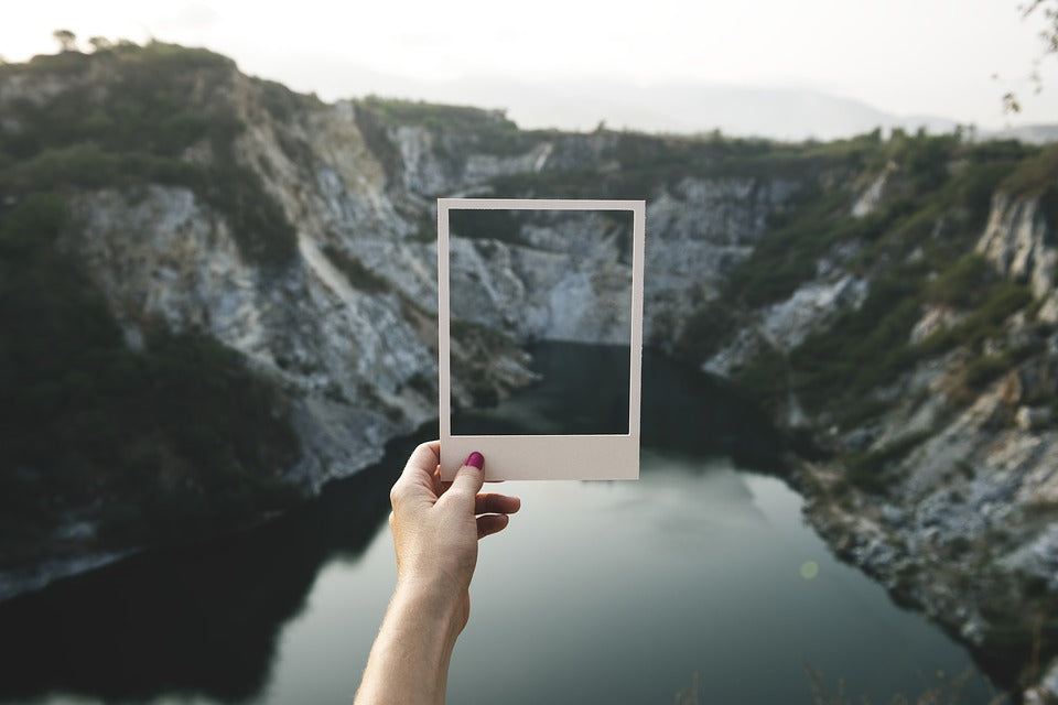 A woman’s hand holding up a white photo frame against a mountain background