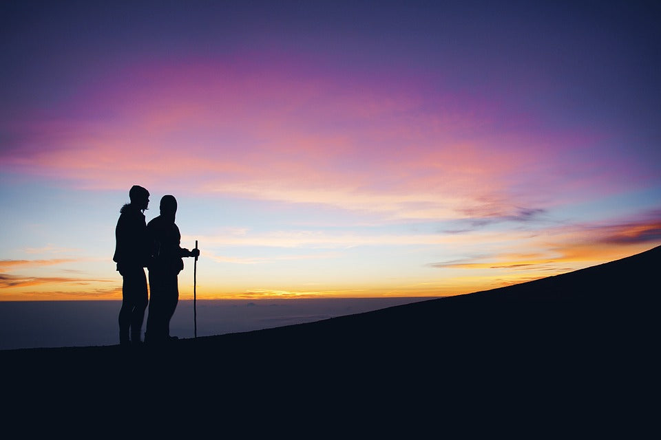 A silhouette of two hikers on a mountain at sunset