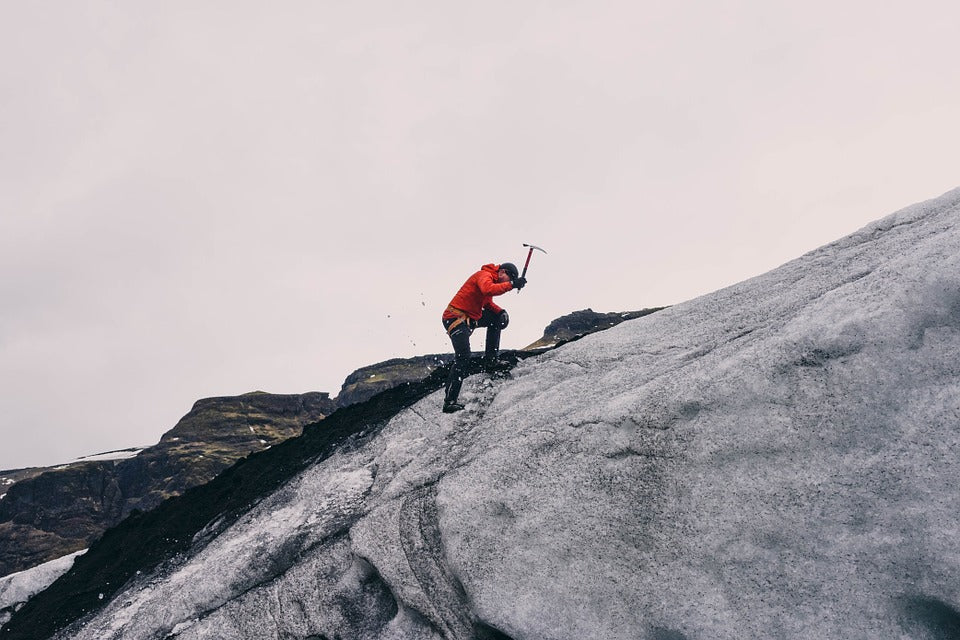 A hiker climbing an icy mountain with an ice pike