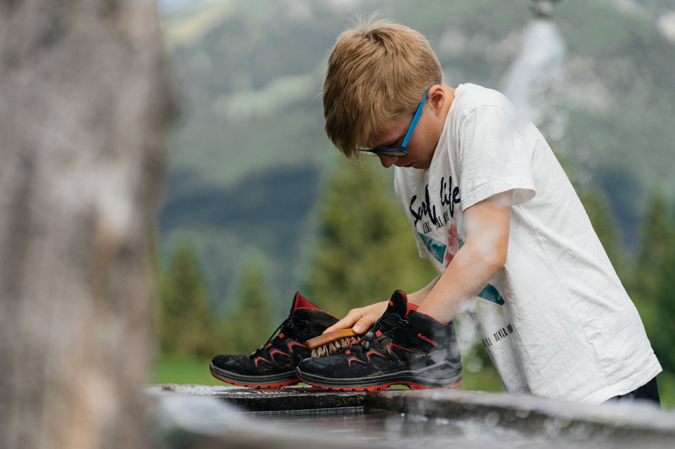 Boy wearing goggles, cleaning walking boots outside. 