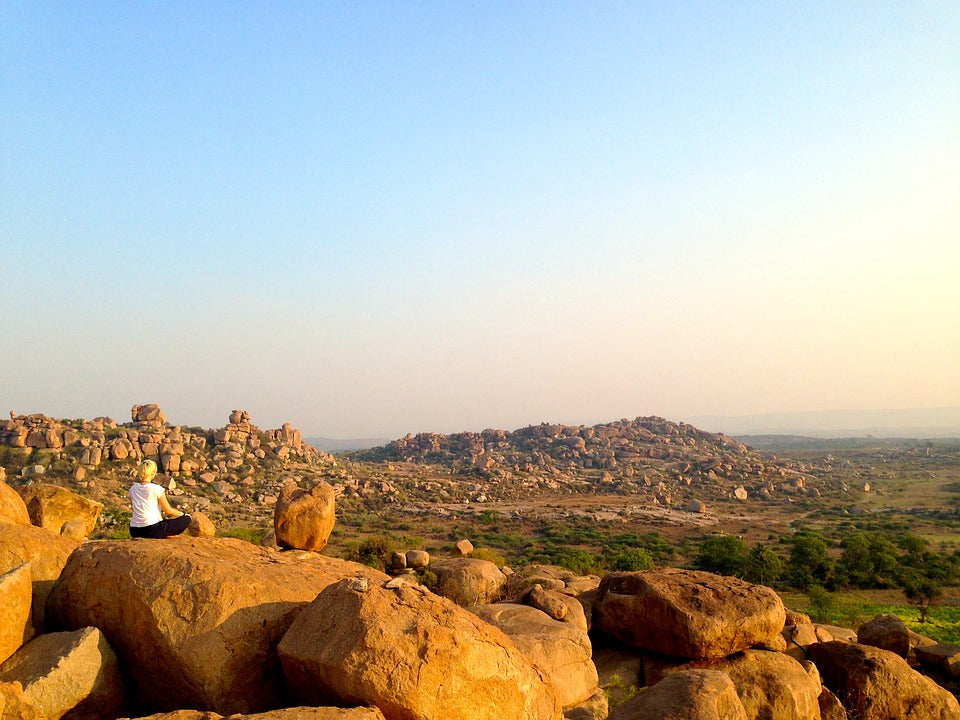 A woman meditating on rocks on a plain on a sunny day