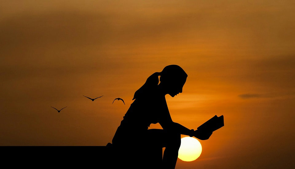 A woman reading a book outside during sunset