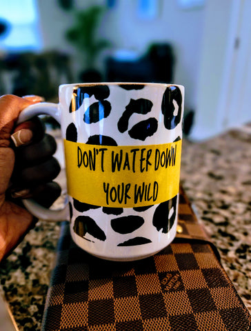 cheetah print coffee mug with yellow banner in the middle and black words that say "Don't water down your wild." The mug is being held by a hand over a brown two tone Louis Vuitton planner