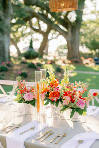Outdoor dining table with plates and cutlery in front of orange floral centerpieces