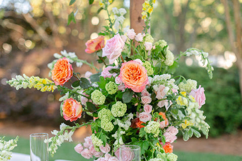 Ornate floral arrangement with pink and orange roses, various greenery, and other light green flowers