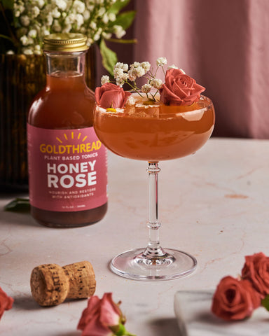 Goldthread Plant-Based Tonics Honey Rose Spritz Cocktail in a coupe glass garnished with roses and chamomile blossoms