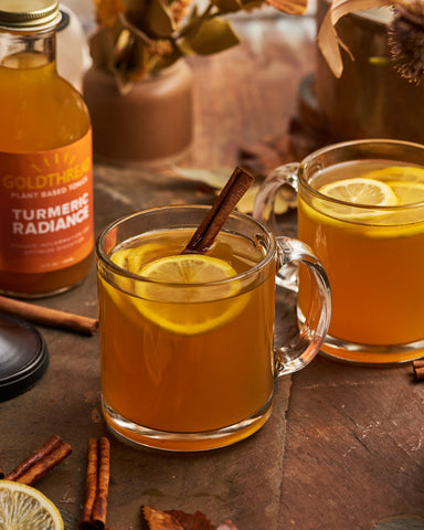 Goldthread Plant-Based Tonics Turmeric Radiance Hot Toddy in a fall setting garnished with lemon slices and cinnamon sticks