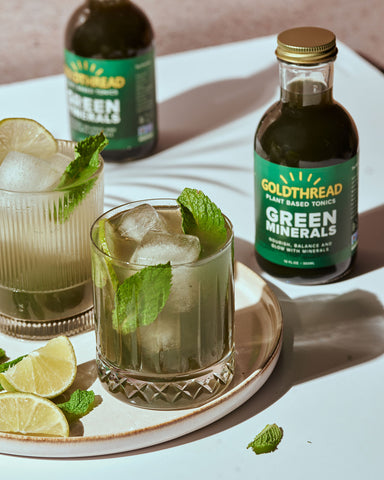 Goldthread Plant-Based Tonics Minty No-Jito mojito mocktail garnished with limes and mint leaves in a rocks glass with ice and Goldthread Plant-Based Tonics Green Minerals tonic