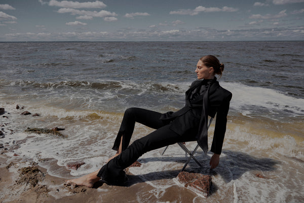 woman wearing black sustainable slow fashion suit in the middle of th ocean
