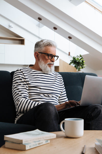 Man With Gray Beard Hair Sitting On Couch Working On Laptop