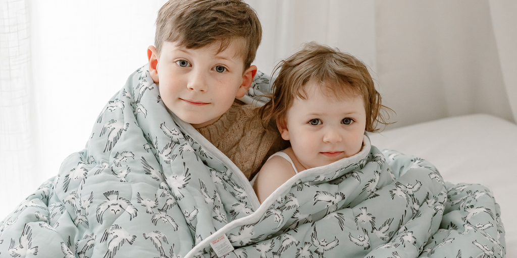 Two kids wrapped in a Nest Designs blanket