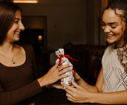 One Person handing a gift in a white bag to another person