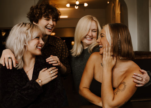 Four people laughing and embracing wearing CONQUERing fidget jewelry