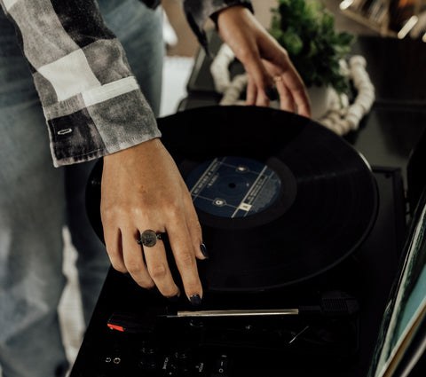 Person putting a vinyl on a record player wearing a black fidget ring.