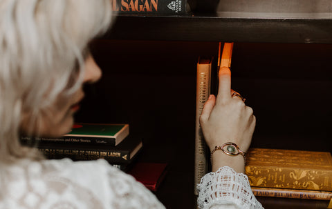 Person pulling a book off a shelf. They are wearing a Rainforest Jasper fidget bracelet