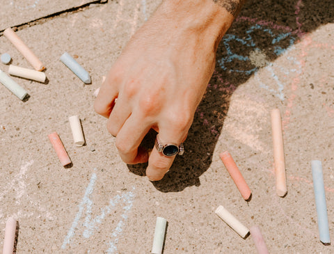 Person coloring with chalk on a sidewalk wearing a fidget ring