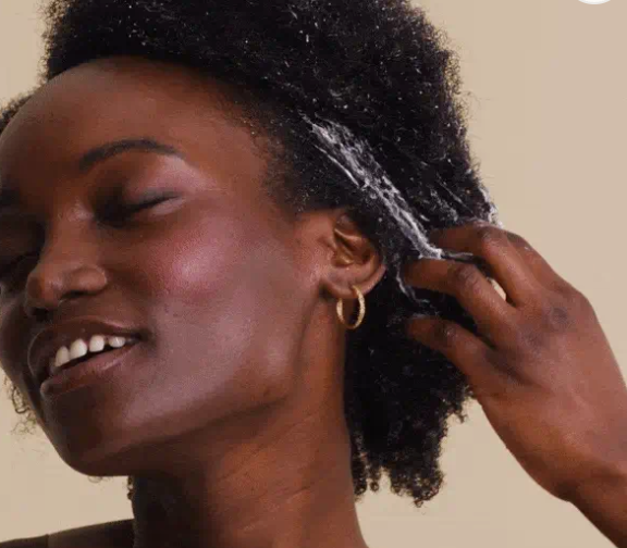 Vrouw met zwart afro-krullend haar die Boucleme's krulcrème gebruikt 