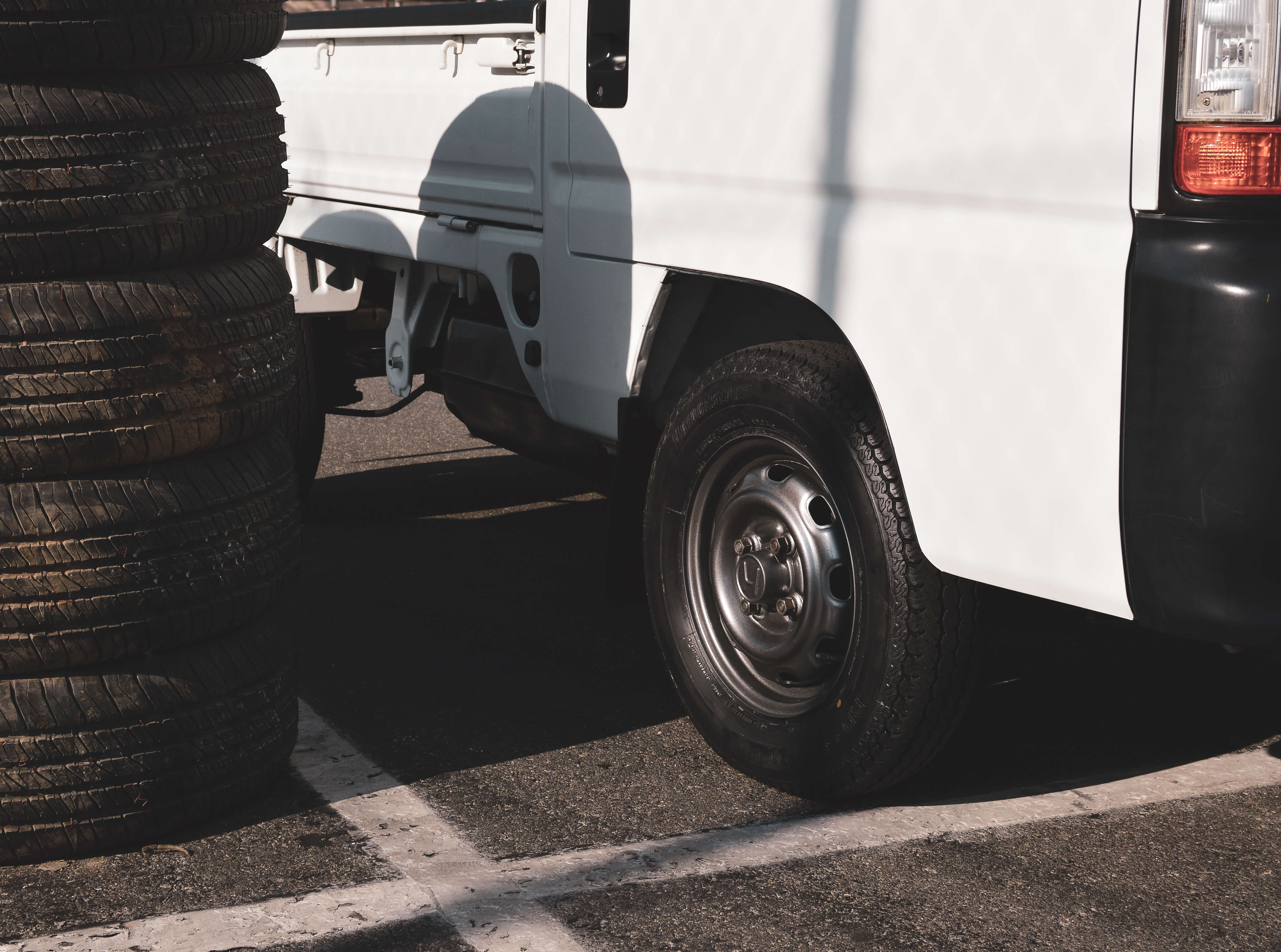 Detail of Honda Acty’s rear steel wheel and tire next to stacked used tires, emphasizing its lightweight yet durable suspension setup.