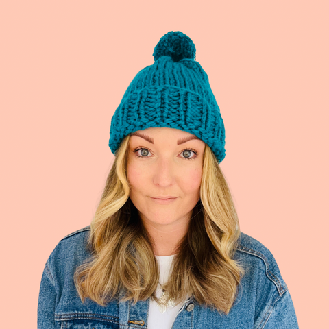 Girl with blonde hair wearing a jade green knitted bobble hat and denim jacket