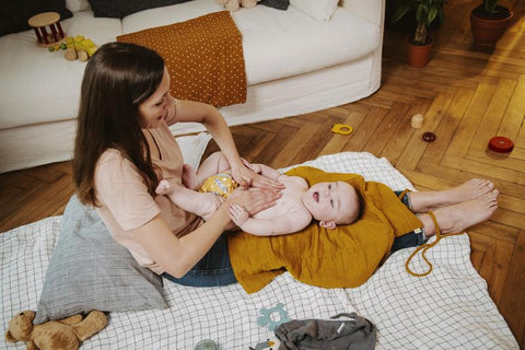 Una madre hace un masaje hidratante a su bebé con el bálsamo de masaje con aceite de aguacate bio