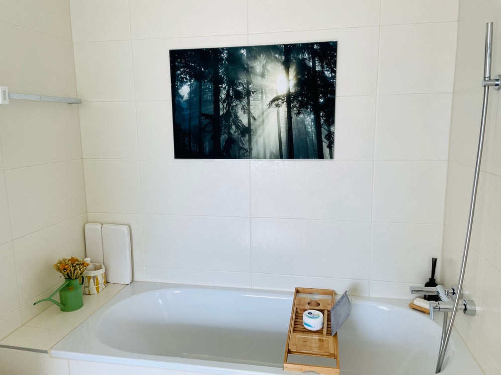 Badewanne mit Trockenblumen-Strauss am Rand, darüber das Bild eines lichtdurchfluteten Waldes