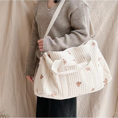 Image d'une femme avec un sac à langer brodé de plusieurs petits oursons, pratique et élégant pour les sorties en famille avec bébé.