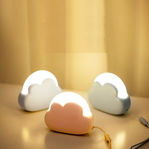Trois mini veilleuses LED nomades en forme de nuage, une blanche, une grise et une rose, émettant une lumière à intensité variable, illustrant la portabilité et la fonctionnalité des veilleuses pour enfants, ainsi que la variété des options de couleur disponibles.