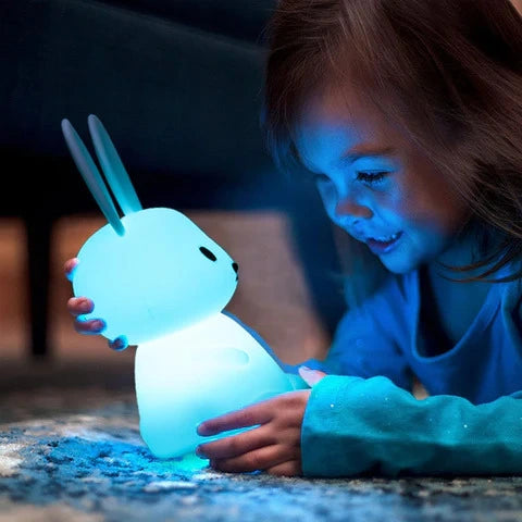 Fille souriante tenant avec amour une veilleuse en forme de lapin illuminée en bleue.