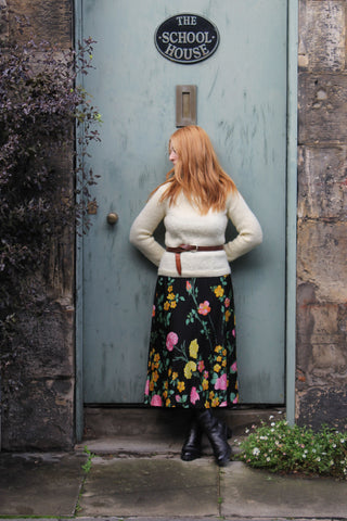 a woman wearing a vintage jumper and a floral skirt leaning against a blue door