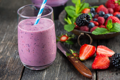 purple berry smoothie in a glass surrounded by fresh strawberries and other dark fruits