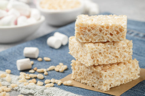 rice krispy treats stacked on a tea towel with ingredients to make them in the background such as marshmallows