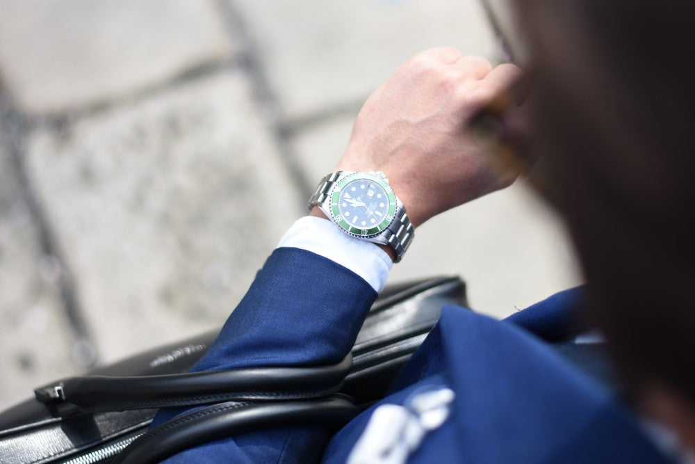 バッグを腕にかけながら腕時計を気にするビジネスマンの写真