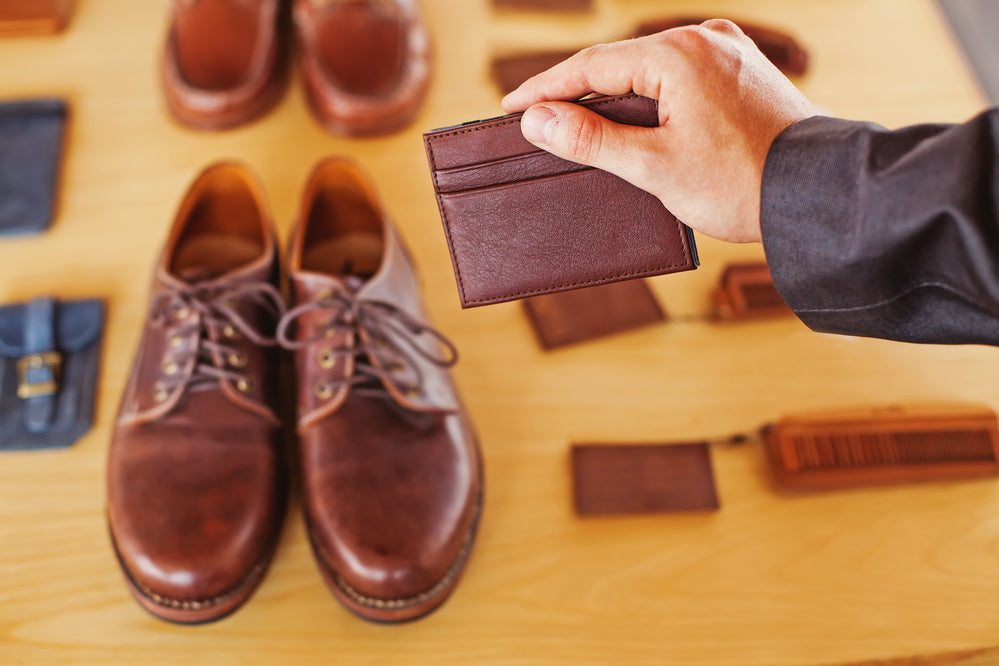 机に並んだ革製品の中から財布を手に取る男性の手元