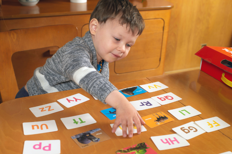 young boy at a table playing a matching game with animal alphabet flash cards