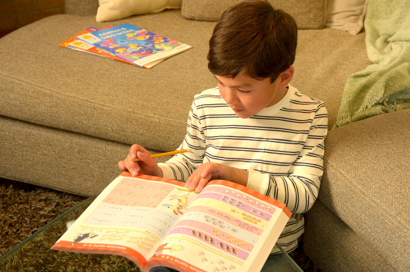 boy sitting at a coffee table working on a school zone math workbook