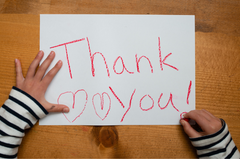 close up of a childs hands as they are writing thank you and some hearts on a piece of white paper