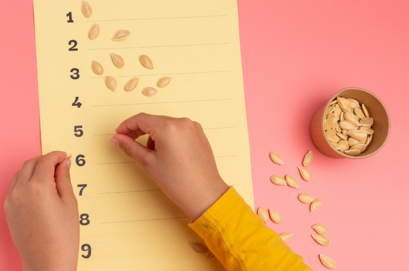 photo of a child placing pumpkin seeds in groups on a piece of paper that has the numbers 1-10 listed 