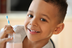 close up of smiling boy with a glass of strawberry milk with a blue and white striped straw sticking out of the glass
