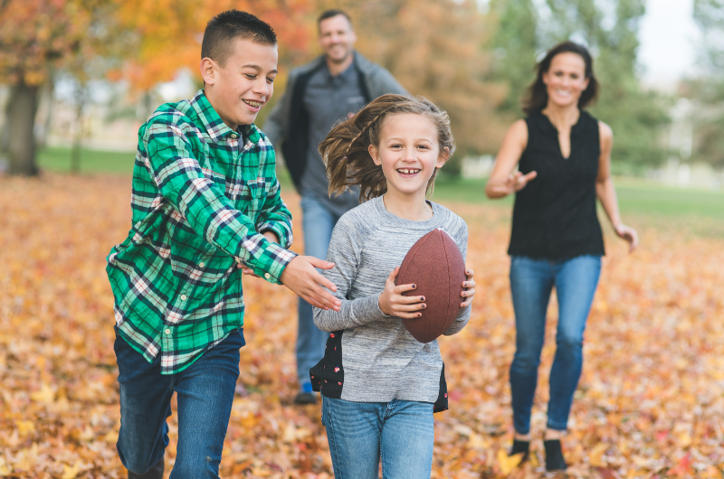 boy, girl, mom and dad running outside in fall playing football together