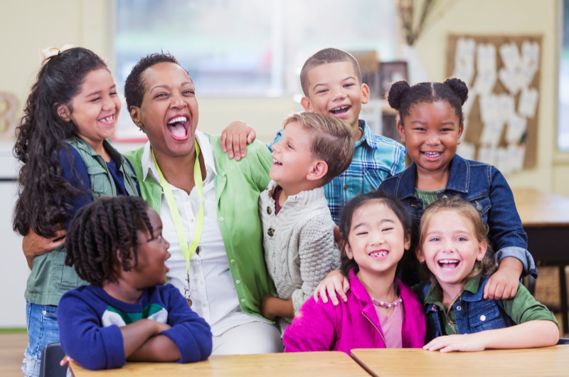 Happy teacher with a classroom group of happy kids gathered around her