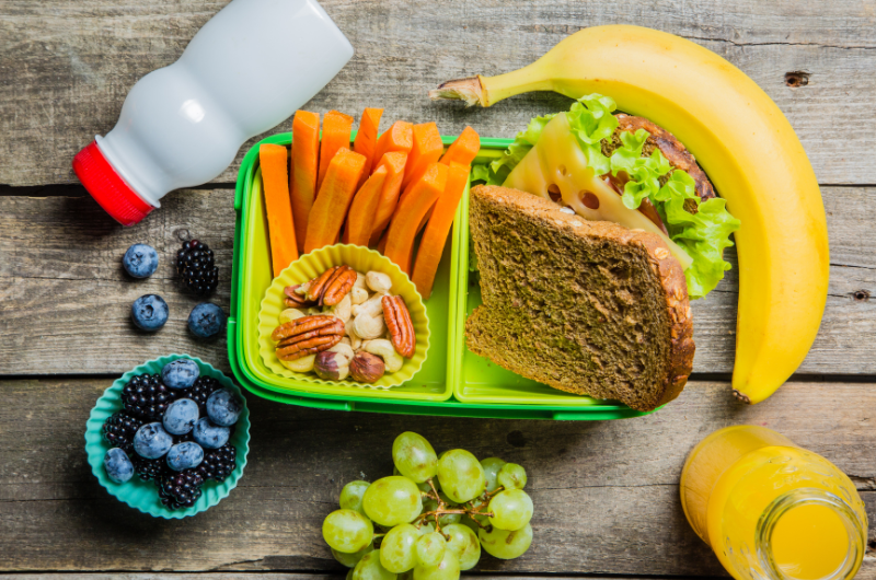 a table with healthy lunch ideas blueberries, carrot sticks, sandwich, banana, grapes nuts juice and milk
