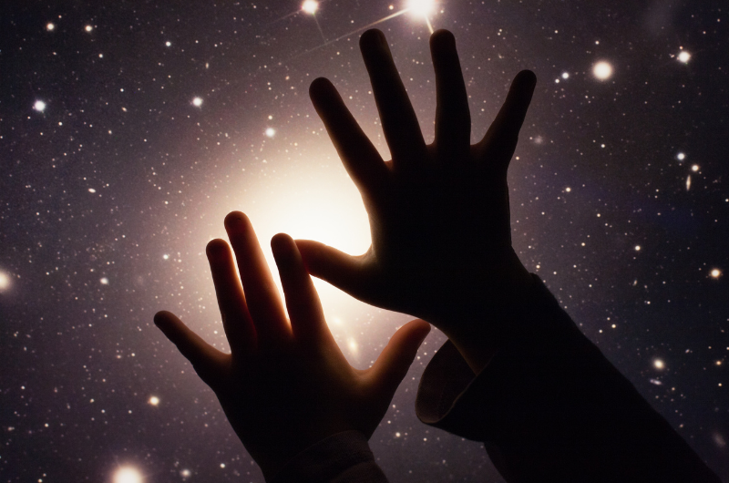 close-up of silhouetted hands of a child in front stars in space background  