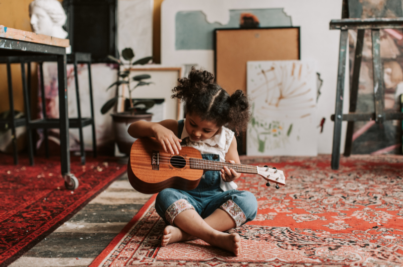little girl sitting on the floor playing a kids size guitar