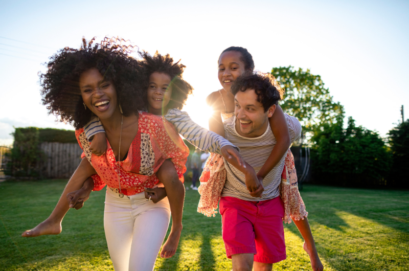 mom and dad giving piggyback rides to their son and daughter super happy enjoying being outside in the sunshine