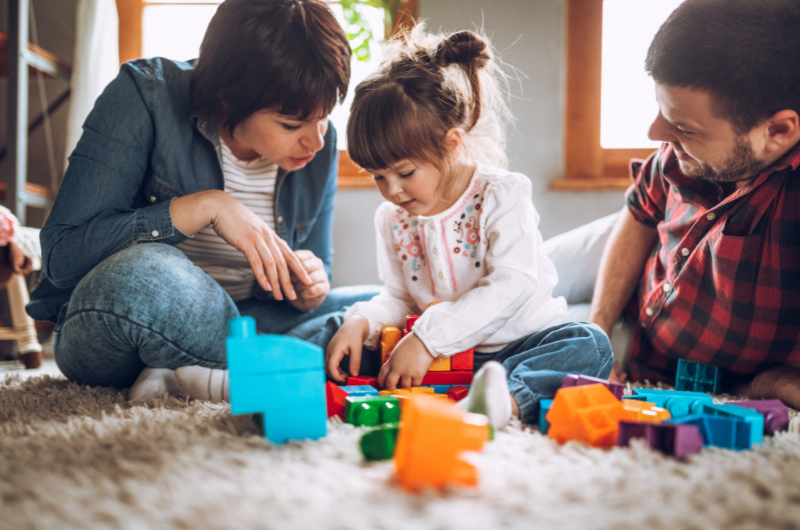 mother and father playing on the floor with blocks with their young child