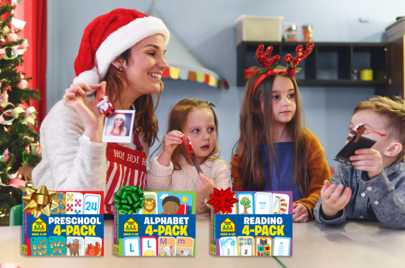 teacher in a classroom wearing a Santa hat with three kindergarten age kids and three packs of school zone 4-pack flash cards in front of them with holiday bows on them