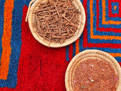 teinture d'herbes dans deux paniers placés sur un tapis de laine teint en rouge avec des plantes