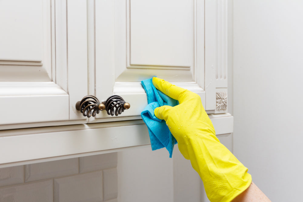 Person in gloves cleaning grease off of kitchen cabinets.