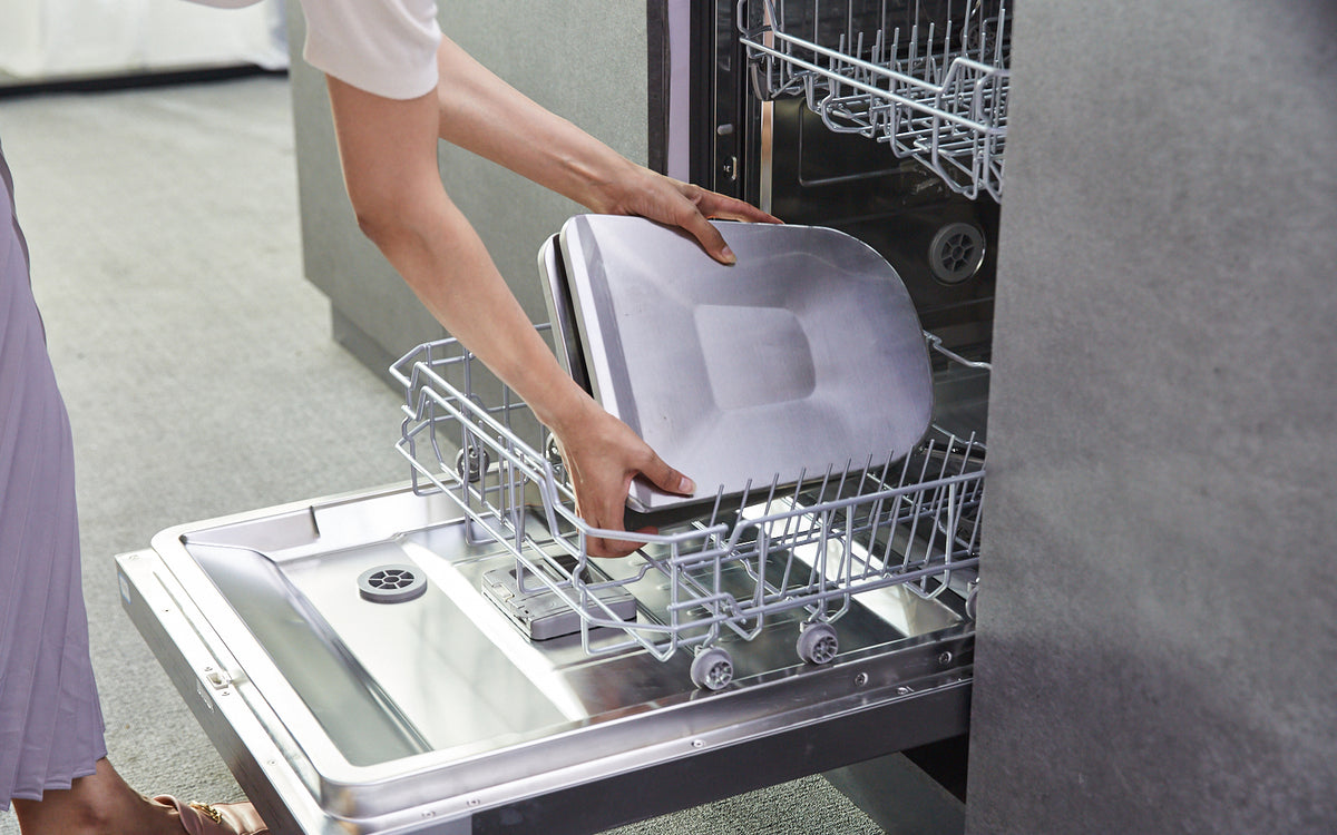 Woman inserting the one-piece capture shield and oil container from the UQS3001 Range Hood into a dishwasher.